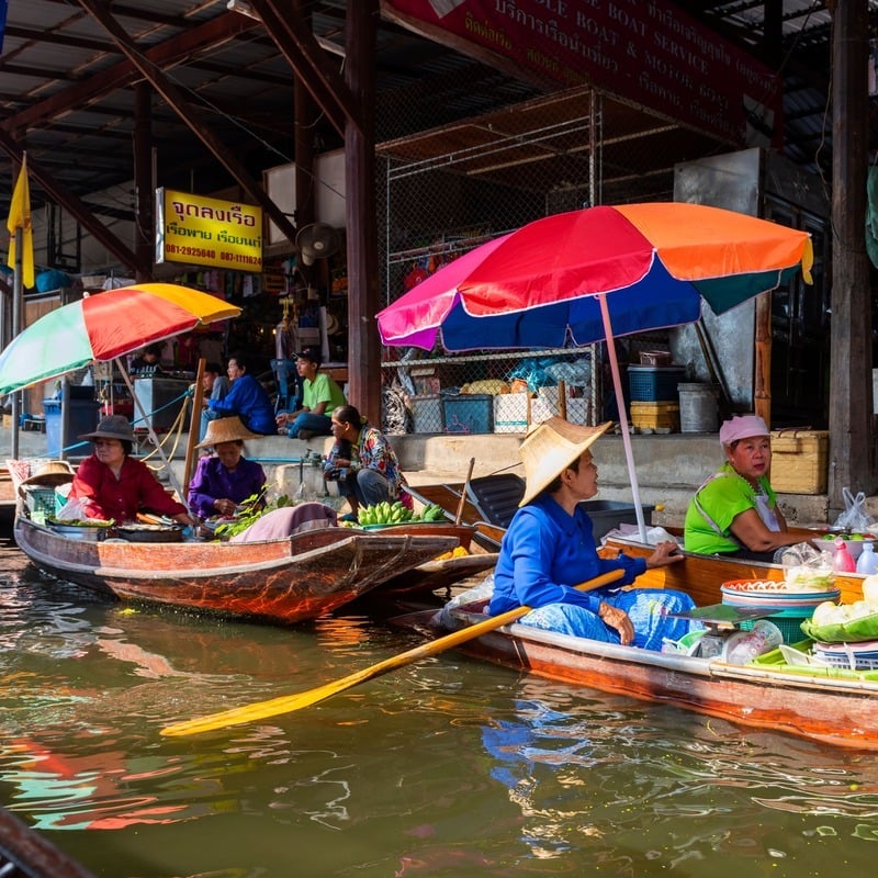 Thai women wearing traditional conical hats as they drive their boats down a canal at a floating market in Thailand, Southeast Asia