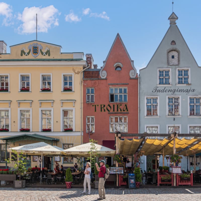The SE facades of the Town Hall Square are colorful restaurants to the right of the yellow Tallinn House of Teachers museum under a blue cloudscape