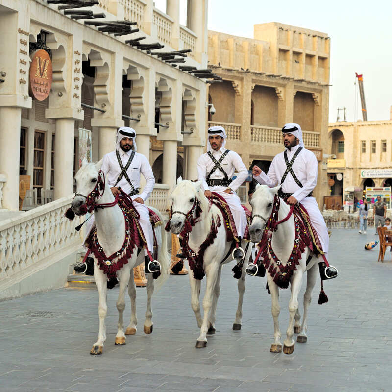 Qatari police officers mounted on horseback and wearing traditional attire in historic Doha, Qatar