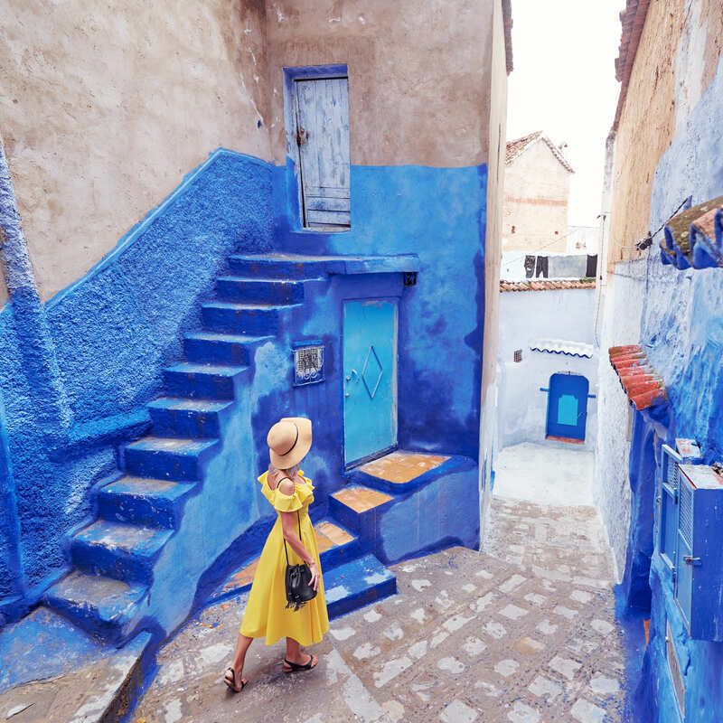 A young woman wearing a yellow dress as she walks through the blue city of Chefchaouen in Morocco, North Africa