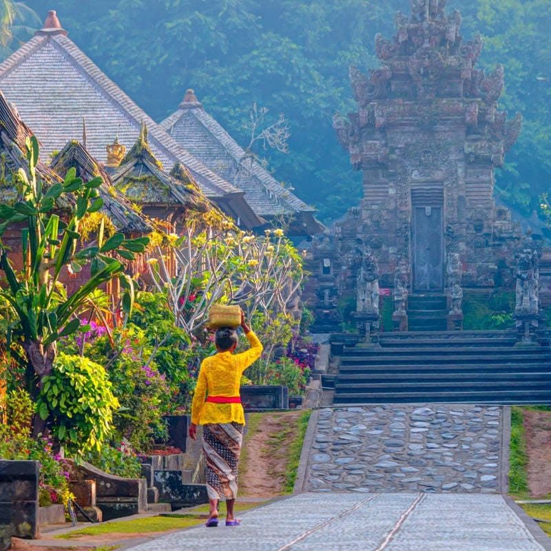 Woman carrying a basket on her head walking towards a temple in Bali