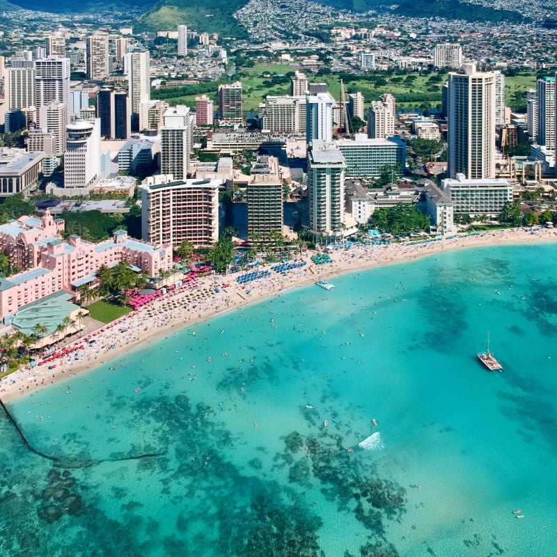 Aerial view of high-rise buildings and waterfront resorts on a small beach with turquoise water