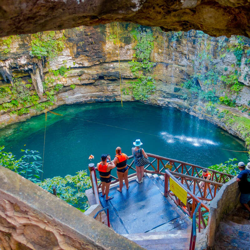 Tourists taking photos of a blue water cenote from an observation point while wearing life jackets, Riviera Maya, Mexico