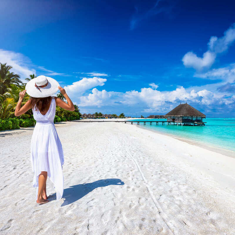 Young woman in a white dress walking along a white sand beach lapped by the Caribbean Sea in an unspecified Caribbean location