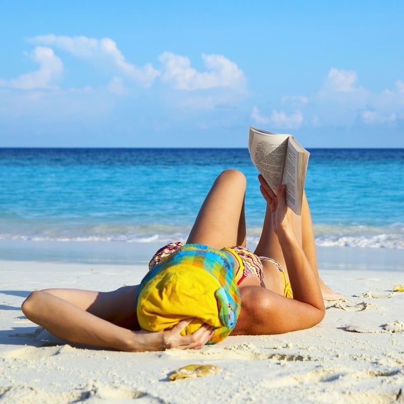 Young Woman Lying On A Sandy Beach In The Caribbean As She Reads A Book, Relaxation Time, Wellness