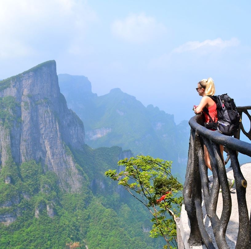 women with a backpack standing on a balcony overlooking the jungle and mountains
